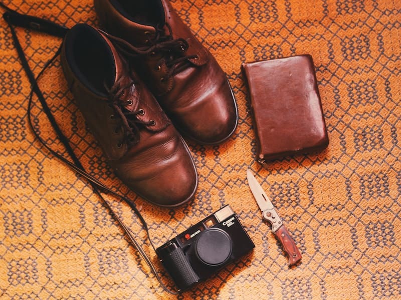 sapatos marrons ao lado de uma faca, de uma camera e de uma carteira
